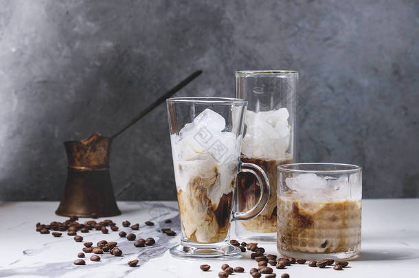冰咖啡鸡尾酒或刨冰与冰块和奶油服务于三不同的眼镜与老式的 jezva 和咖啡豆周围的白色大理<strong>石桌</strong>子与灰色混凝土墙背景.