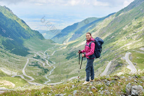 微笑的<strong>女性游客</strong>站在与步行坚持到美丽的景色华丽缠绕 Transfagarashan 路在罗马尼亚。女子登山者青山山快乐岩石旅游路线路径