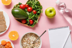 新鲜饮食食品的顶视图,空白笔记本与铅笔和水在粉红色背景