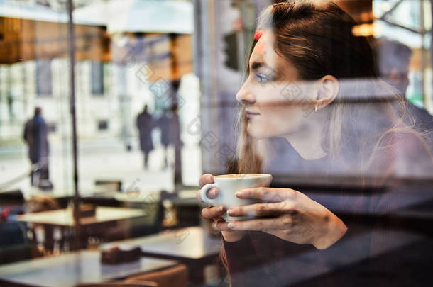 女孩在当地咖啡店拿着咖啡杯做白日梦, 通过窗户制作概念照片, 让城市效果与反思