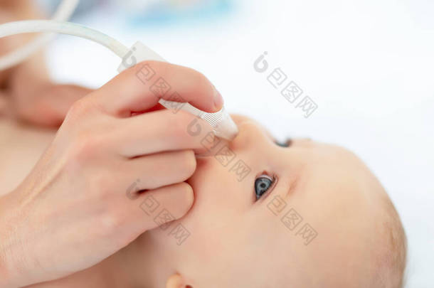 小宝宝的妈妈用吸气器和医疗工具在家里为可爱的男婴擦拭流鼻涕。婴儿父母保健和爱的概念