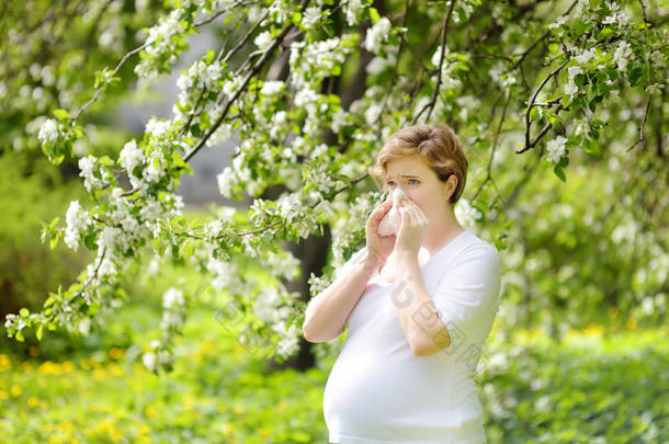 孕妇在春天公园散步时打喷嚏，用餐巾擦鼻子。流感季节，感冒鼻炎。过敏的人.