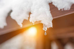 屋顶上融化的雪冰柱的特写。水滴下降。春天的开始。满足冷、热的概念。清新的春天自然背景