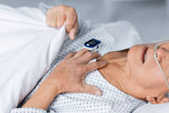 头戴鼻腔导管和脉搏血氧计的老年病人躺在床上的临床观察