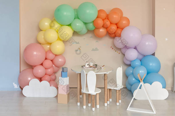 小桌子和椅子，小兔子耳朵在儿童房的内部。彩虹，五彩缤纷的气球拱门，节日、<strong>生日</strong>、<strong>宴会</strong>的装饰品