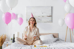 在卧室里用智能手机和香槟微笑庆祝生日的女人