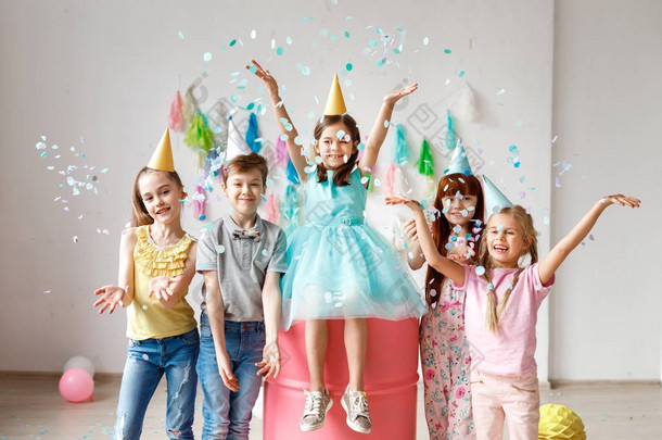 可爱的孩子们一起玩, 扔五颜六色的五彩纸屑, 戴圆锥帽, 在生日聚会上玩, 在不同的游戏中一起玩耍, 花时间在装饰的房间里。儿童与活动概念
