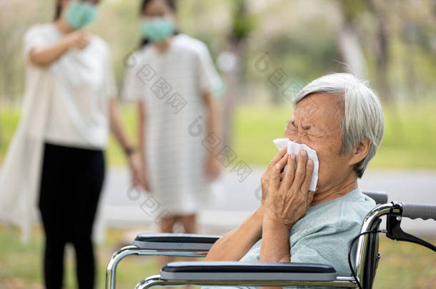 亚洲老年生病妇女流鼻涕，打喷嚏发烧，感染流感症状，眼镜蛇-19，大肠癌，两个戴面具的人，避免与病人接触，保持距离