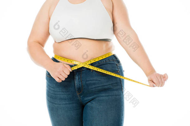 穿着牛仔裤测量腰围的超重妇女的裁剪视图, 在白色上隔离测量胶带, 减肥的概念
