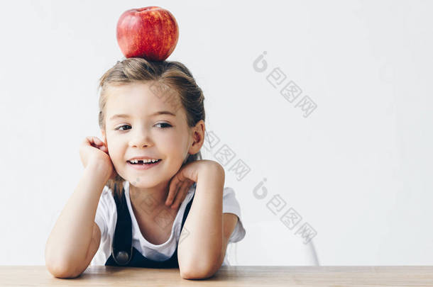 <strong>小女生</strong>坐在桌子上, 红苹果在头上孤立的白色