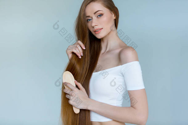 脱发的概念。照片中的年轻女子，有着长长的干枯的棕色头发，背景是灰色的，很不快乐，很有压力.
