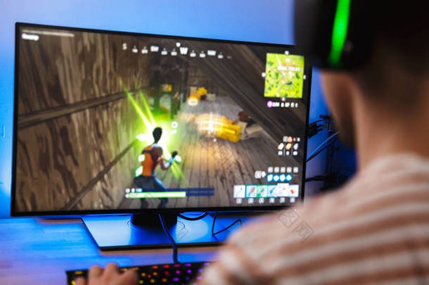 在家里坐在桌边的玩家在电脑上玩电子游戏的后视图