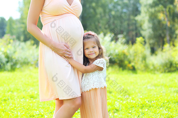 Happy pregnant woman, cute little child daughter hugging mother