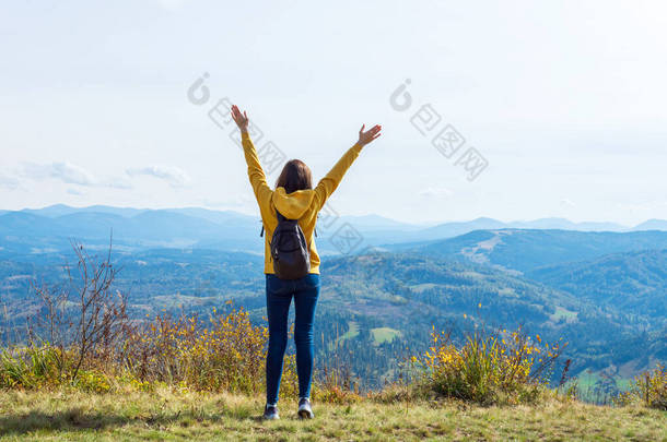穿着黄色帽衫的女孩，双手高举，<strong>站在山顶</strong>上。成功。旅行情况.