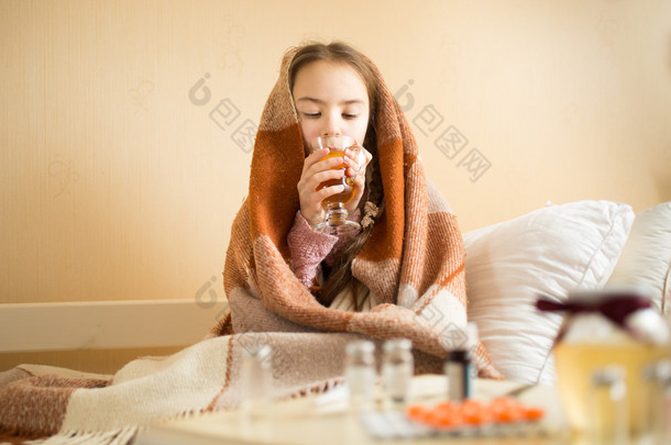 Portrait of sick girl covered in blanket drinking hot tea