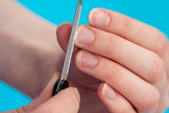 一个高加索女人的手，用蓝色背景的指甲文件擦亮她的指甲，特写。指甲、手的自我保健的理念