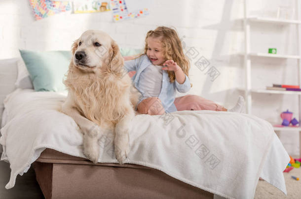 快乐可爱的孩子在儿童房的床上拍下金毛猎犬