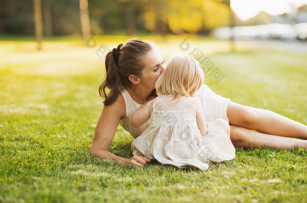 妈妈亲吻婴儿坐在公园的草地上