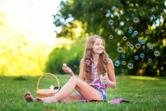 年轻的女孩坐在吹泡泡的草地上