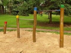 在儿童游乐场的木柱子上的横向钢筋。橙色砂下面在背景中的酒吧，绿色公园.