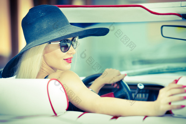 户外夏天的驾驶一辆<strong>敞篷</strong>车的红色复古时尚复古美女的画像。时尚迷人金发女性，红色汽车的黑帽子。阳光明亮的颜色，在户外拍摄.