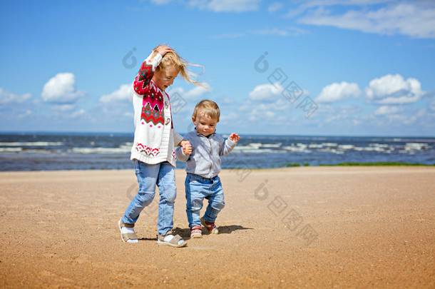 姐姐和哥哥年轻金发沿着海滩散步，手牵手，打击海.