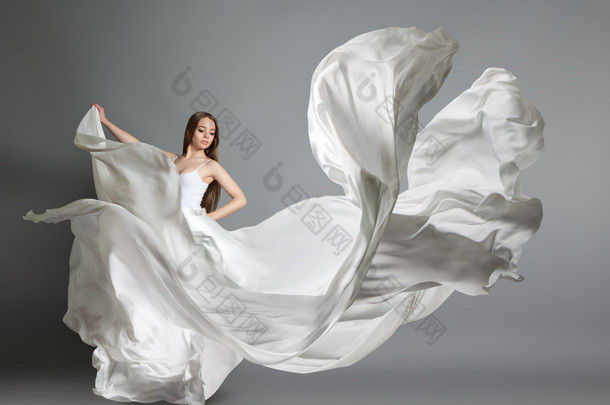 美丽的年轻姑娘跳舞。中飞白色连衣裙的女孩。白色的布料在空中飞翔。白色的光穿衣服