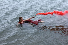 年轻美貌淹没了发烟手榴弹后船浮在水面上的红衣的女人.