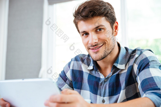 快乐的年轻人穿花格子衬衫，在家里使用平板电脑
