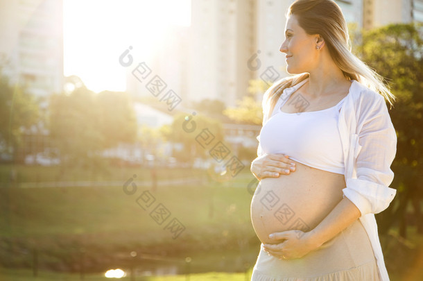 美丽的孕妇在日落在公园外