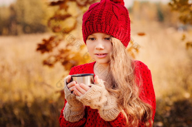 快乐的孩子女孩在暖红色针织的帽和围巾上舒适的秋天从<strong>热水</strong>瓶走<strong>喝</strong>热茶。季节性的户外活动