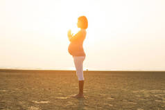 怀孕的母亲在海滩上表演瑜伽