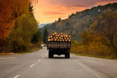旧卡车满载木原木旅行低谷保加利亚道路，秋季日落时间