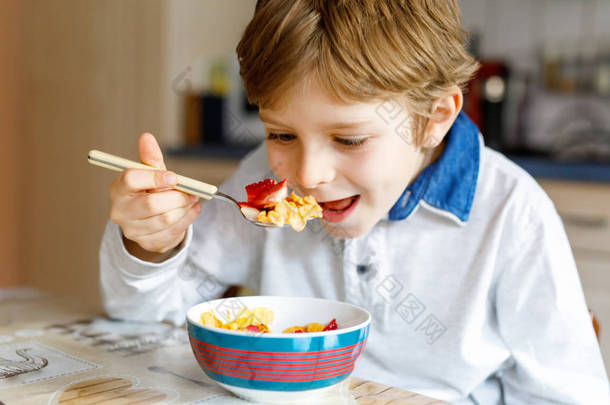 <strong>早饭</strong>吃谷物与牛奶和浆果、 新鲜草莓的小金发学校孩子男孩
