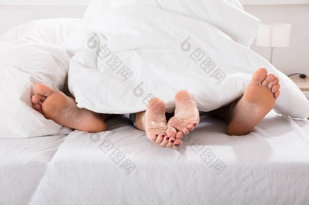 男性和女性的双腿，在床上的床单下