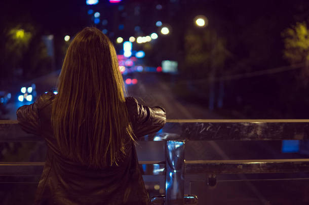 年轻女子看视图夜间城市道路从桥