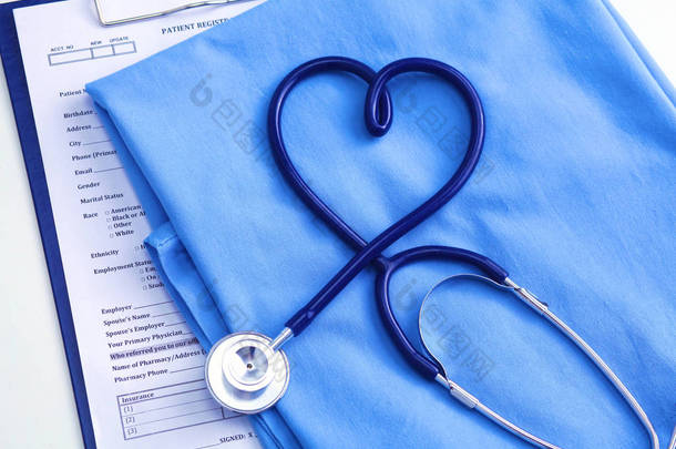 医用听诊器扭曲心形躺在病人医疗历史记录列表和蓝色医生统一特写