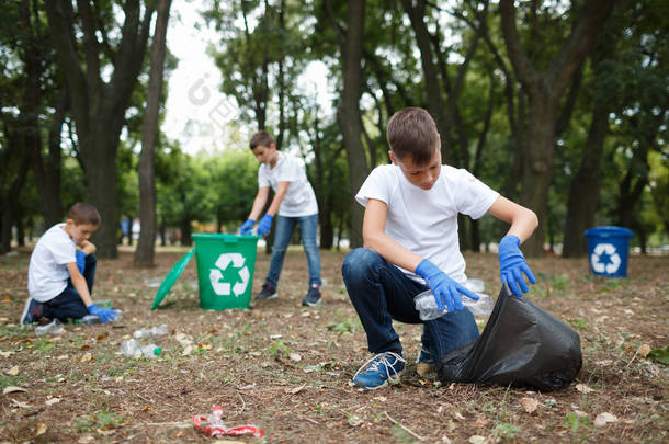 小孩捡垃圾和放在黑色的垃圾袋里自然的背景。生态保护的概念.