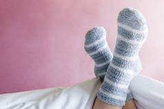 放松和舒适的概念, 女性脚在温暖的条纹羊毛袜子在床上, 粉红色粉彩作为背景墙