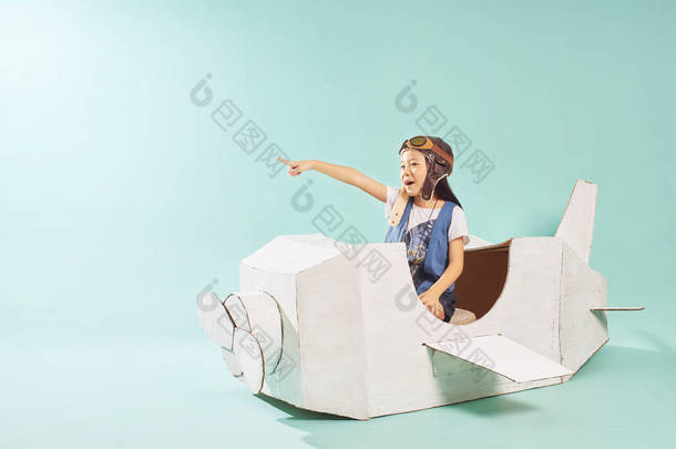 小可爱的女孩玩纸板飞机。白色复古风格的纸板飞机上薄荷绿色背景。童年梦想想象概念 .