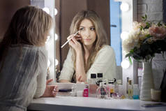 神奇的年轻女子在镜子前化妆。化妆品桌旁漂亮姑娘的画像