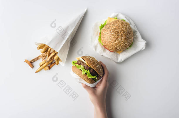 女性手的裁剪视图与汉堡包和薯条在纸锥, 隔离在白色