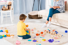 用平板电脑拍摄的女人, 而小儿子在家玩玩具