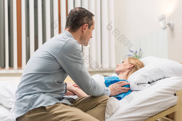 丈夫坐在生病的妻子<strong>病床</strong>在医院