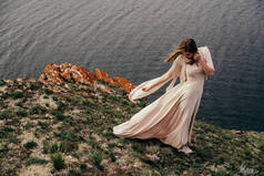 在草地上穿着白色连衣裙的年轻女孩。女人穿着漂亮的长裙在草地上摆姿势