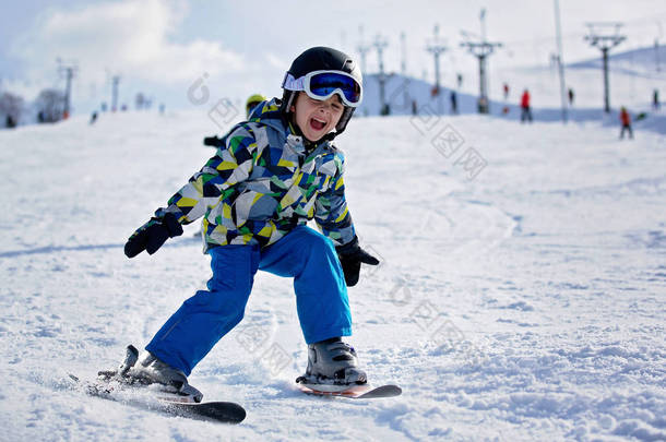 可爱的小学龄前儿童在蓝色夹克, 愉快地滑雪在