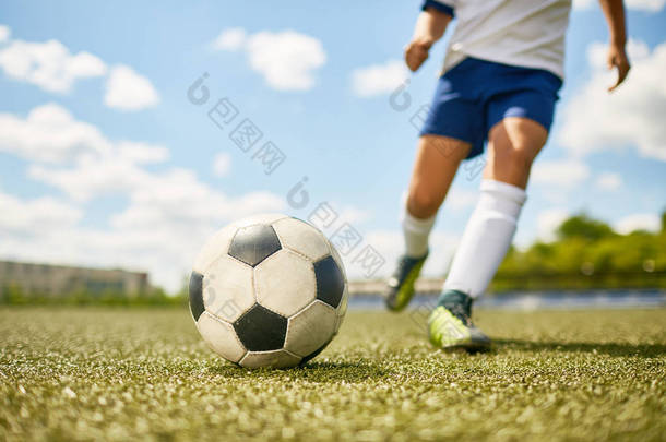 低剖面肖像的不识别青少年男孩踢球在足球场练习, 专注于足球躺在草地上