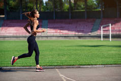 年轻的健身妇女在体育场跑道上奔跑。在体育场训练的运动员女孩做锻炼。健康活跃的生活方式.