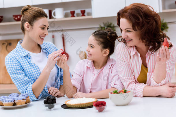 三代欢笑的妇女一起在厨房装饰甜点与浆果一起