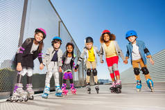 大群青春期的孩子, 快乐的在线溜冰者在防护装备, 站在一排牵手在体育场户外